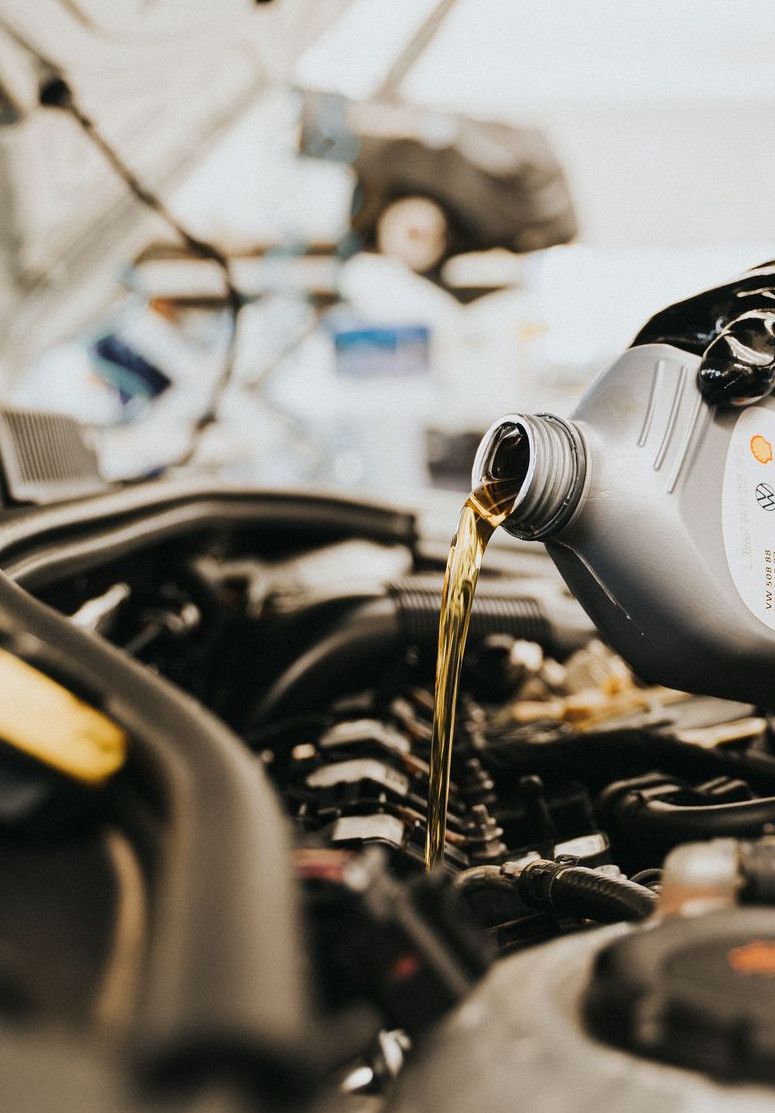 Close-up of a mechanic pouring engine oil into a car engine in an auto repair shop.